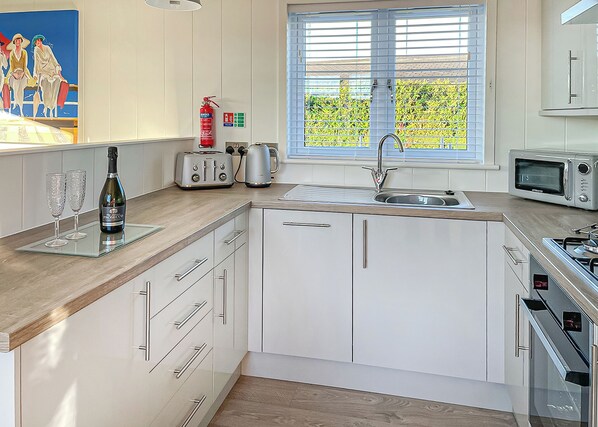 A modern kitchen with white cabinets, a stainless steel sink, a toaster, a kettle, and a microwave.
