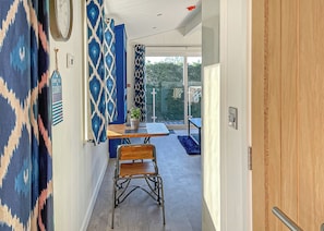 A hallway with patterned curtains, a wooden chair, a table with a potted plant, and a sliding glass door leading to an outdoor area. - New for 2022. Fabulous one bedroom lodge with super king-size bed. (Easingwold)