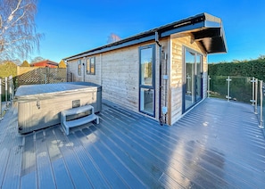 A modern wooden cabin with a hot tub, deck, and glass doors.