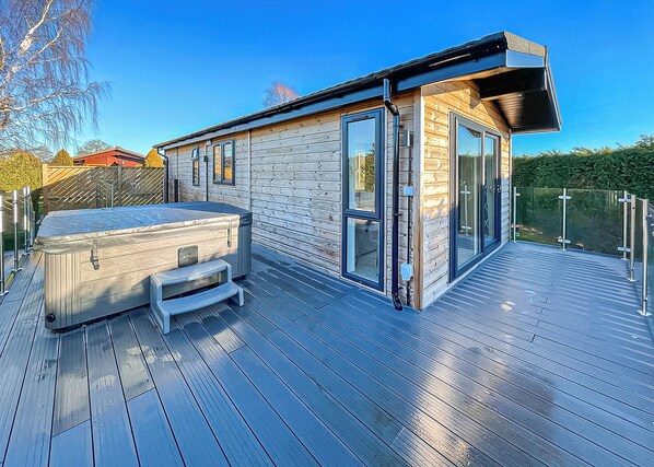 Una cabaña de madera moderna con jacuzzi, terraza y puertas de cristal.
