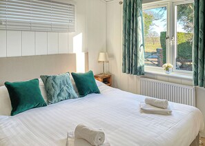 Una cama bien hecha con almohadas, una lámpara de noche y una ventana con cortinas.