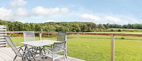 A deck with a table and chairs overlooking a grassy field.