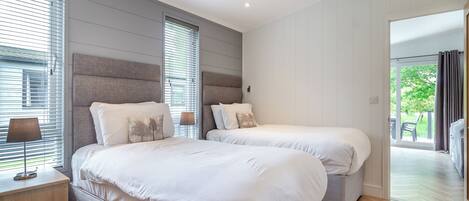 A modern bedroom with two beds, a bedside table, a lamp, and a view of the outdoors.