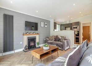 A modern living room with a fireplace, sofa, coffee table, and kitchen area.
