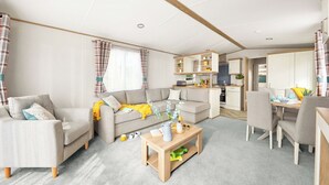 A modern living room with a sofa, coffee table, and dining area. - Stylish and modern caravan with one double and one twin. (Clarach Bay, Nr Aberystwyth)