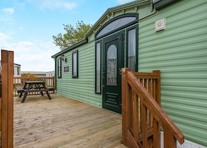 A green mobile home with a wooden deck, a picnic table, and a door with a window.