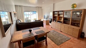 A living room with a sofa, a dining table with chairs, a TV, a bookshelf, and a globe on the wall. - Carvoeiro Terrace - Gorgeous apartment close to beach (Carvoeiro)