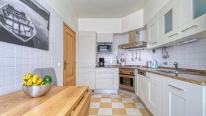 A modern kitchen with white cabinets, a microwave, an oven, and a sink. There is a wooden table with a bowl of fruit on it. - Carvoeiro Terrace - Gorgeous apartment close to beach (Carvoeiro)