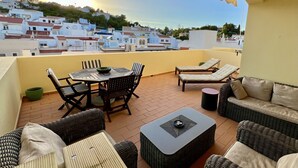 A balcony with wicker furniture, a round table, and a view of a town with white buildings. - Carvoeiro Terrace - Gorgeous apartment close to beach (Carvoeiro)