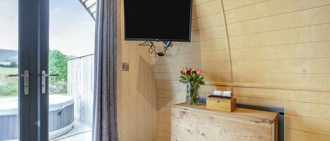 Un interior de madera con puerta corredera de vidrio, televisor montado, cómoda de madera y un florero con flores.