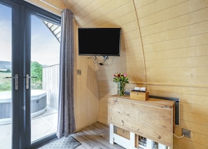 Un interior de madera con puerta corredera de vidrio, televisor montado, cómoda de madera y un florero con flores.