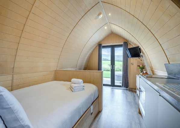 Ein gemütliches Zimmer mit einem Bett, einer kleinen Küchenzeile, einem Fernseher und einer Schiebetür zu einem Außenbereich.