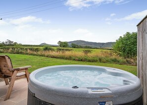 A hot tub with a wooden chair, a wooden deck, and a view of a grassy field with hills in the background. - 1 bedroom accommodation in Great Busby (Great Busby)