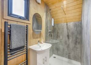 A bathroom with a wooden vanity, a round mirror, a towel rack, a shower, and a window. - 1 bedroom accommodation in Great Busby (Great Busby)