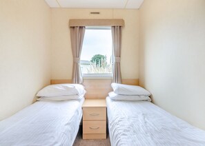 Ein kleines Hotelzimmer für Einzelpersonen mit zwei Betten, einem Fenster mit Vorhängen, einem hölzernen Kopfteil und einem Deckenlüfter.