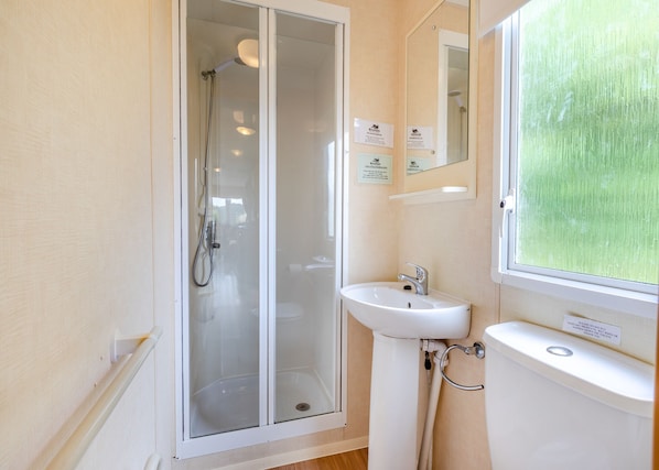 Een badkamer met een douchecabine van glas, een wastafel en een toilet.