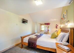 Une chambre à coucher avec un lit, une table de chevet, une télévision, une fenêtre et des rideaux.