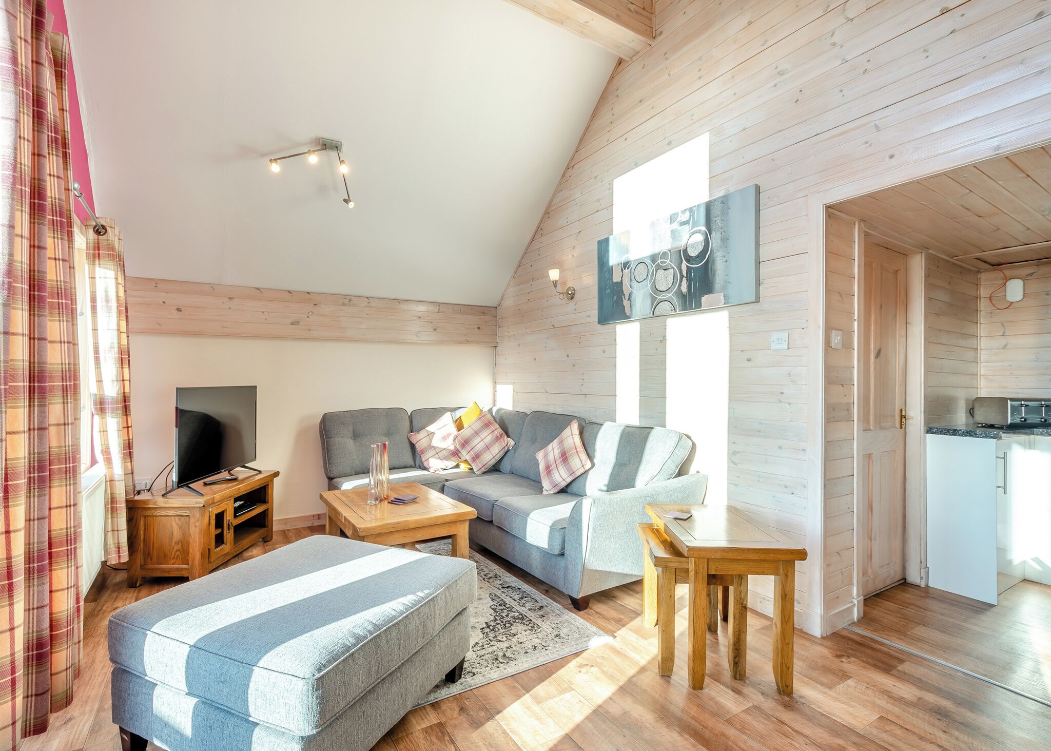 Un salon confortable avec un canapé, un pouf, une table basse en bois et un téléviseur à écran plat.