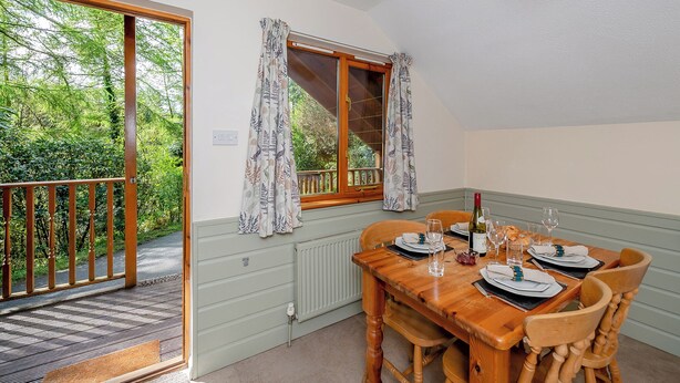 A dining area with a table set for two, a window with curtains, and a view of greenery outside.