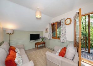 Una sala de estar con televisión, sofá, mesa y ventana con cortinas.