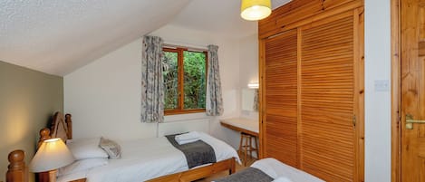 Une chambre avec deux lits, une armoire en bois, un bureau avec une chaise, une fenêtre avec des rideaux et un luminaire au plafond.