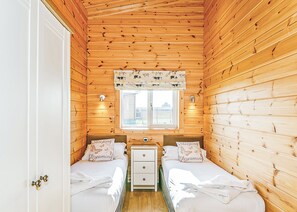 Una habitación tipo cabaña con paredes de madera, un ventanal con vistas, dos camas con almohadas a juego y una mesita de noche pequeña.