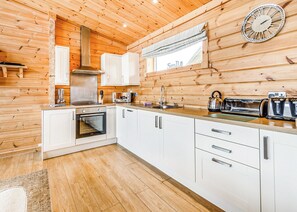 Une cuisine moderne avec des murs en bois, des armoires blanches, une hotte de cuisinière en acier inoxydable, un four à micro-ondes, une bouilloire et une horloge.