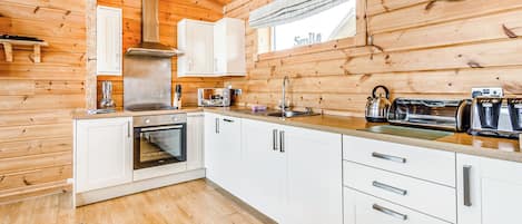 Une cuisine moderne avec des murs en bois, des armoires blanches, une hotte de cuisinière en acier inoxydable, un four à micro-ondes, une bouilloire et une horloge.