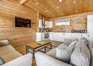 L’intérieur chaleureux d’un chalet comprend un salon, un canapé, une table basse, un coin cuisine et un téléviseur fixé au mur.