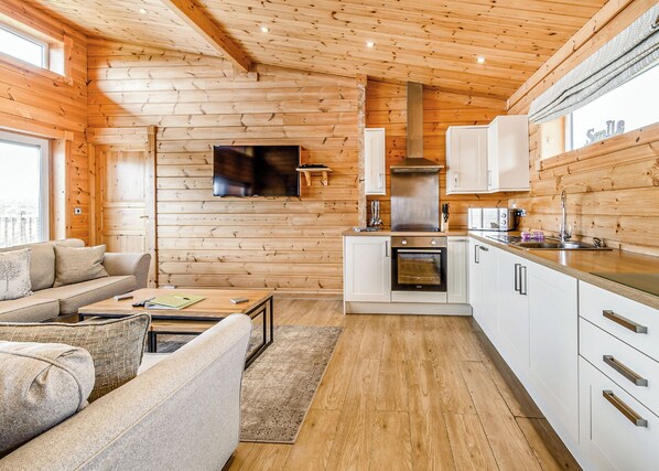 Un interior acogedor de cabaña con sofá, mesa de centro, televisor, zona de cocina y paredes de madera.