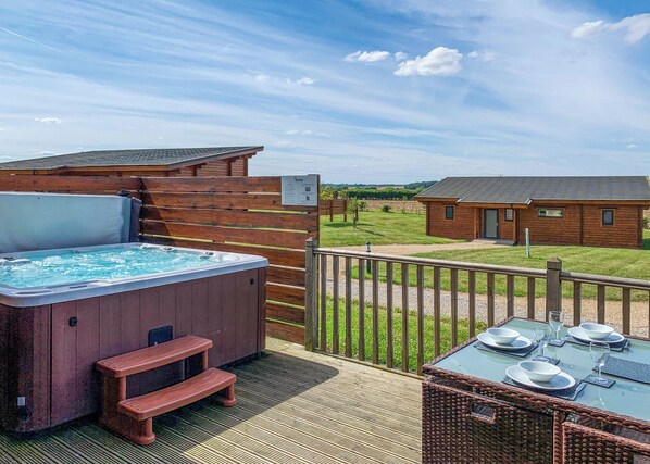 A hot tub, wooden deck, outdoor table with chairs, and a wooden cabin in the background.