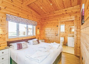 A wooden cabin bedroom with a bed, bedside tables, a window, and a bathroom.