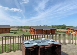 A wooden deck with a table set for dining, overlooking a row of cabins.