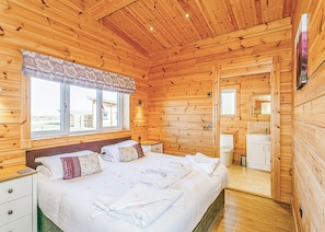 Un dormitorio de cabaña de madera con cama, mesitas de noche, una ventana y un baño.