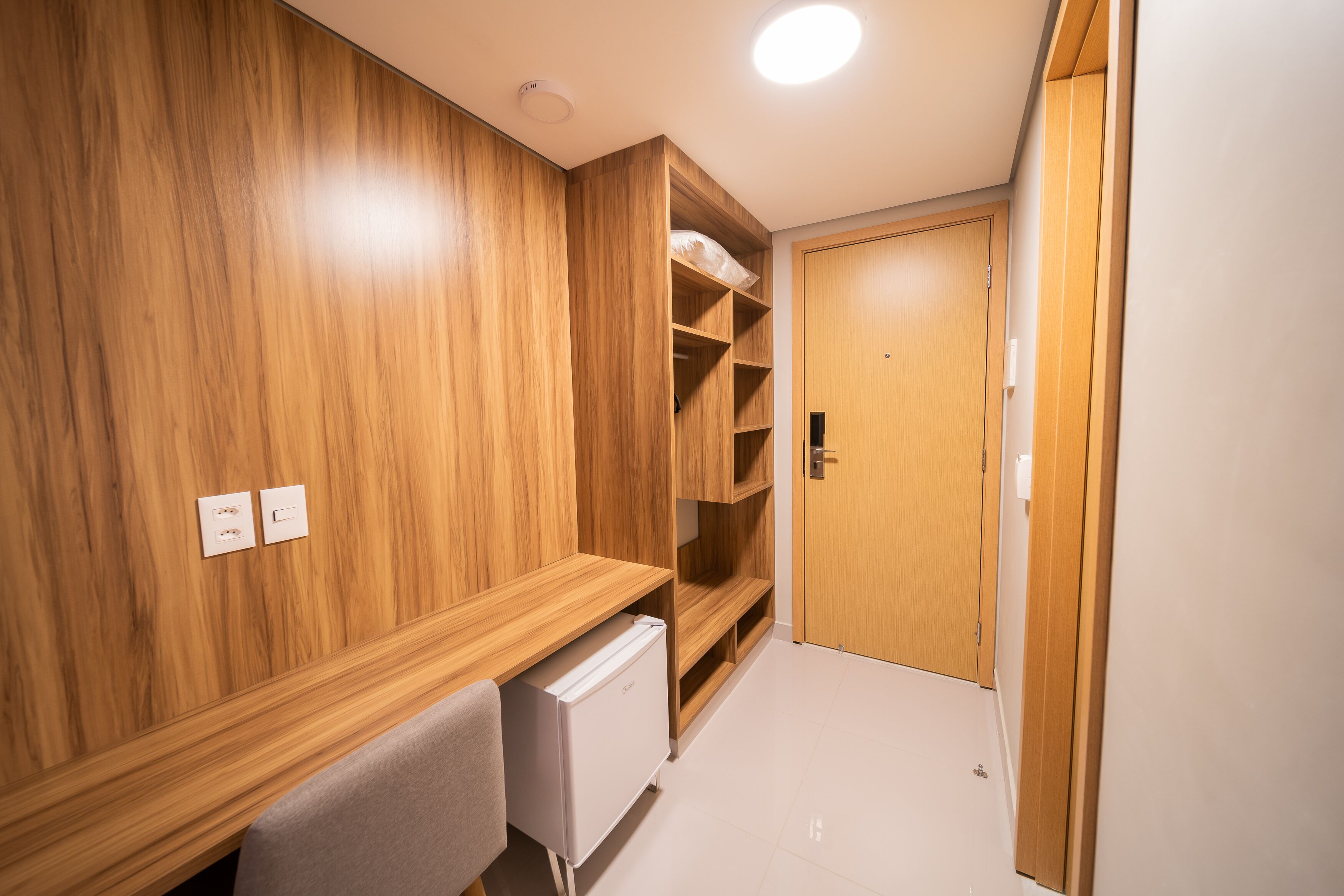 A compact room with wooden paneling, a built-in desk, a white radiator, and a door leading to another room.