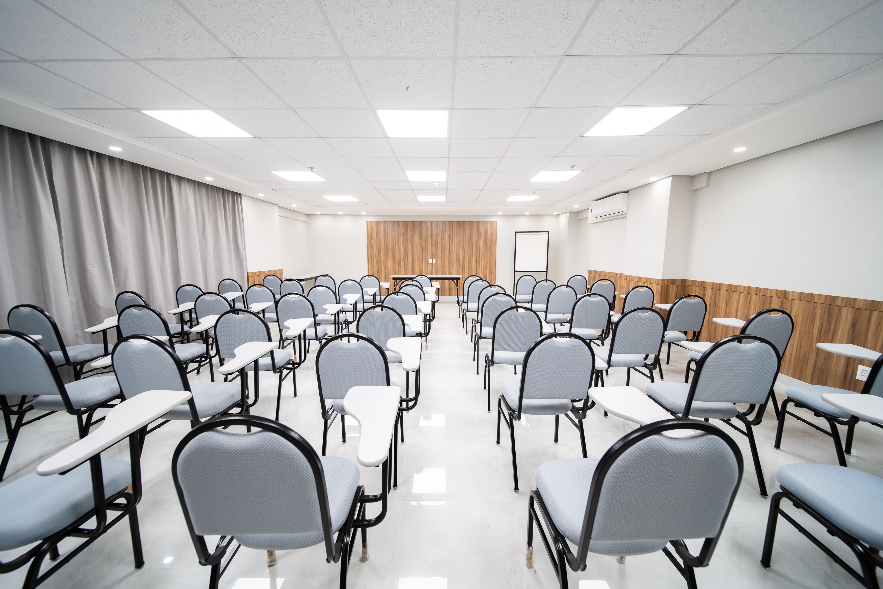 A conference room with rows of chairs and tables, a wooden panel wall, and a whiteboard.