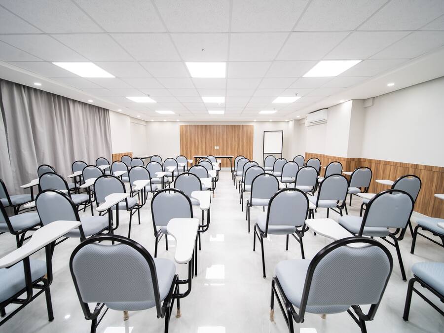 Un salón de conferencias con filas de sillas y mesas, un panel de pared de madera y una pizarra.