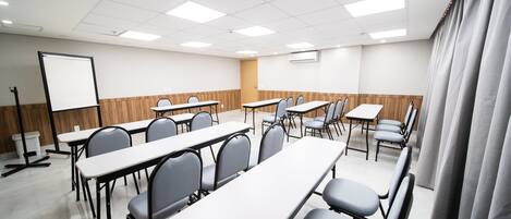 Un salón de conferencias con mesas y sillas, una pizarra y una pantalla de proyector.
