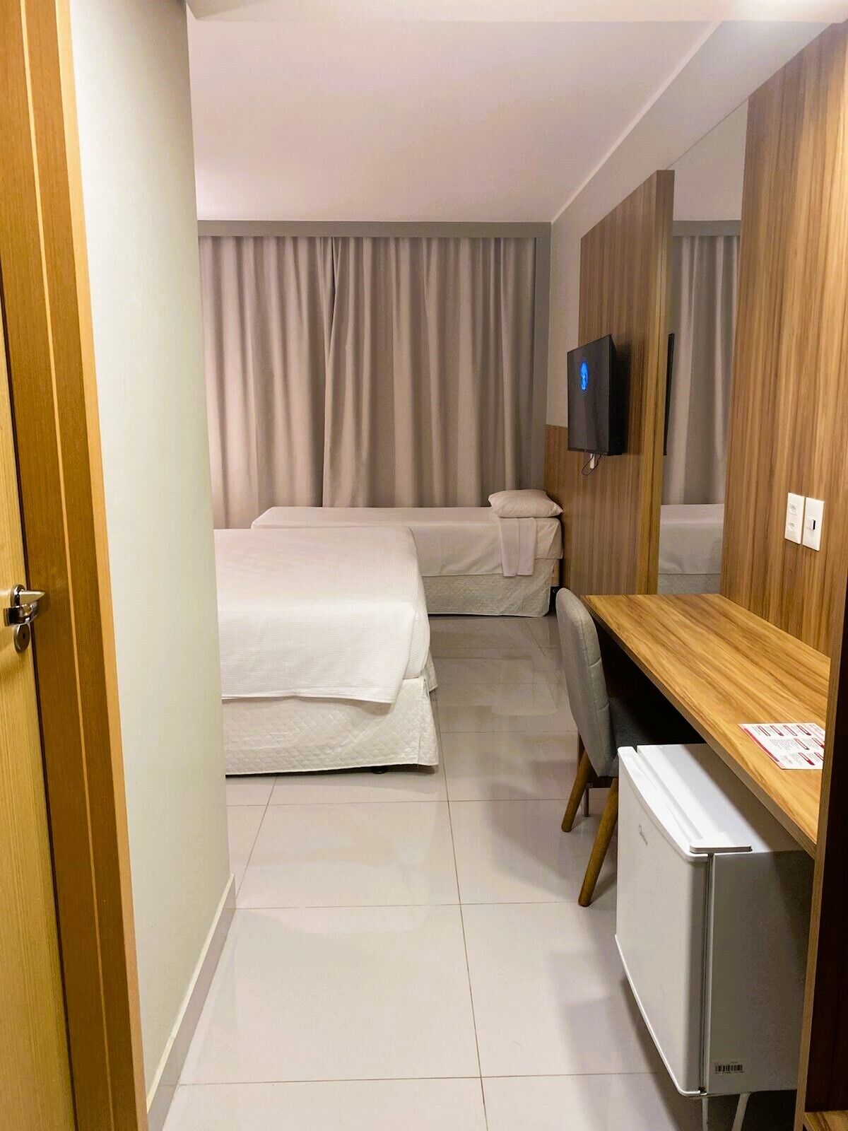 A hotel room with two beds, a desk, a television, and a refrigerator.