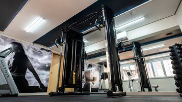 Un gimnasio con equipamiento de ejercicio, un espejo grande y un cartel de una persona haciendo ejercicio.