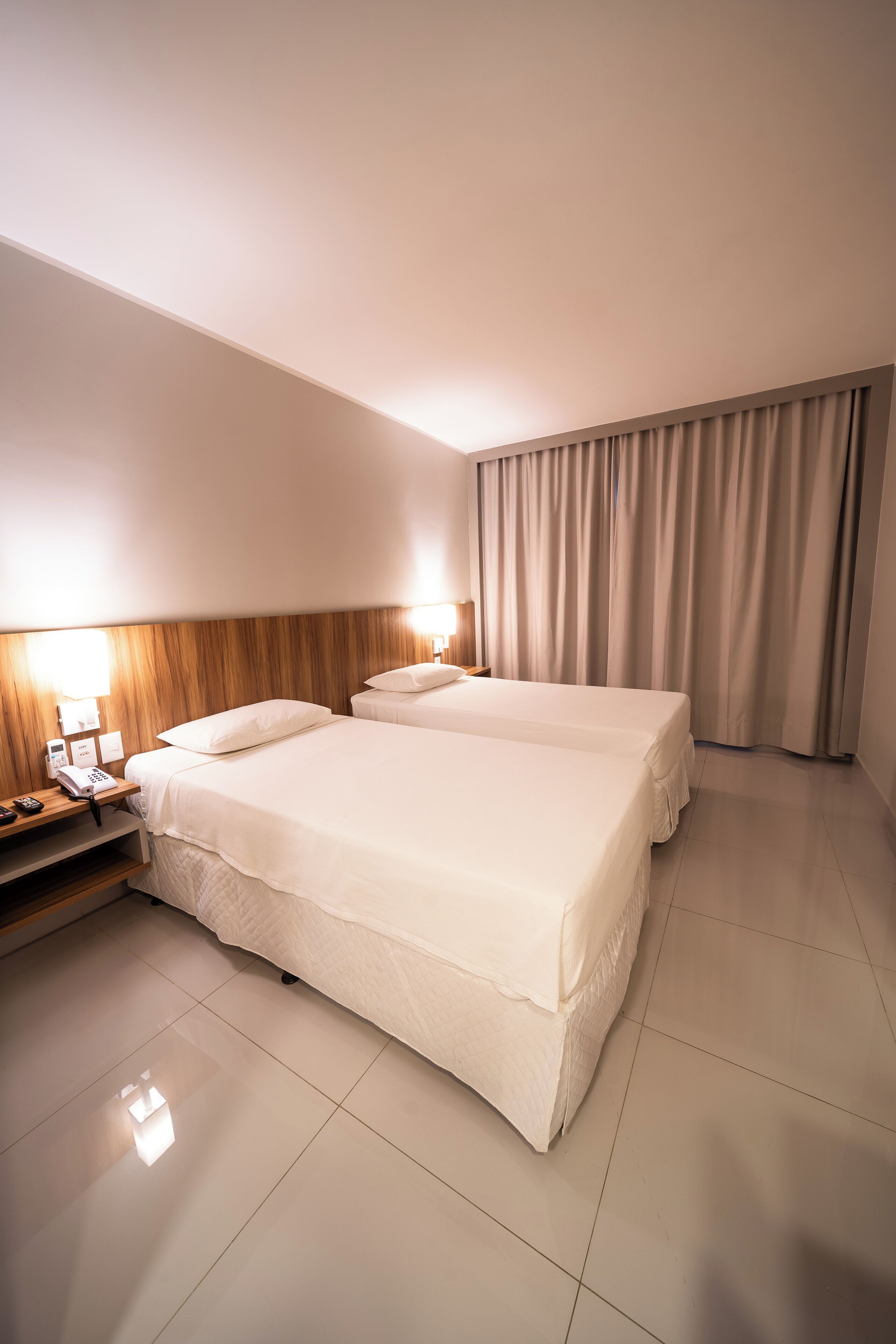 Habitación de hotel con dos camas, una mesita de noche con lámpara, un teléfono y una cortina.