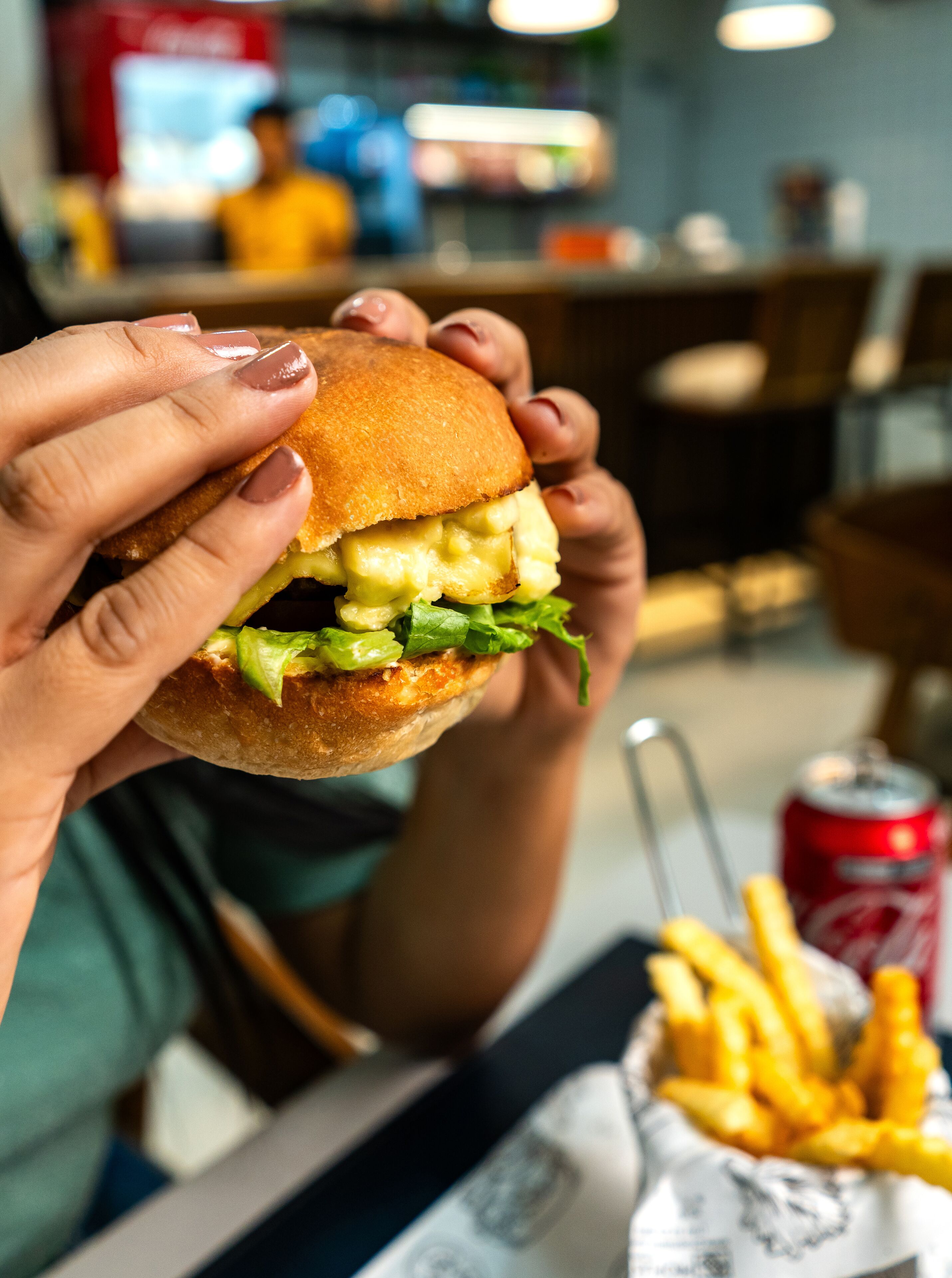 A person holding a burger with visible lettuce and cheese.