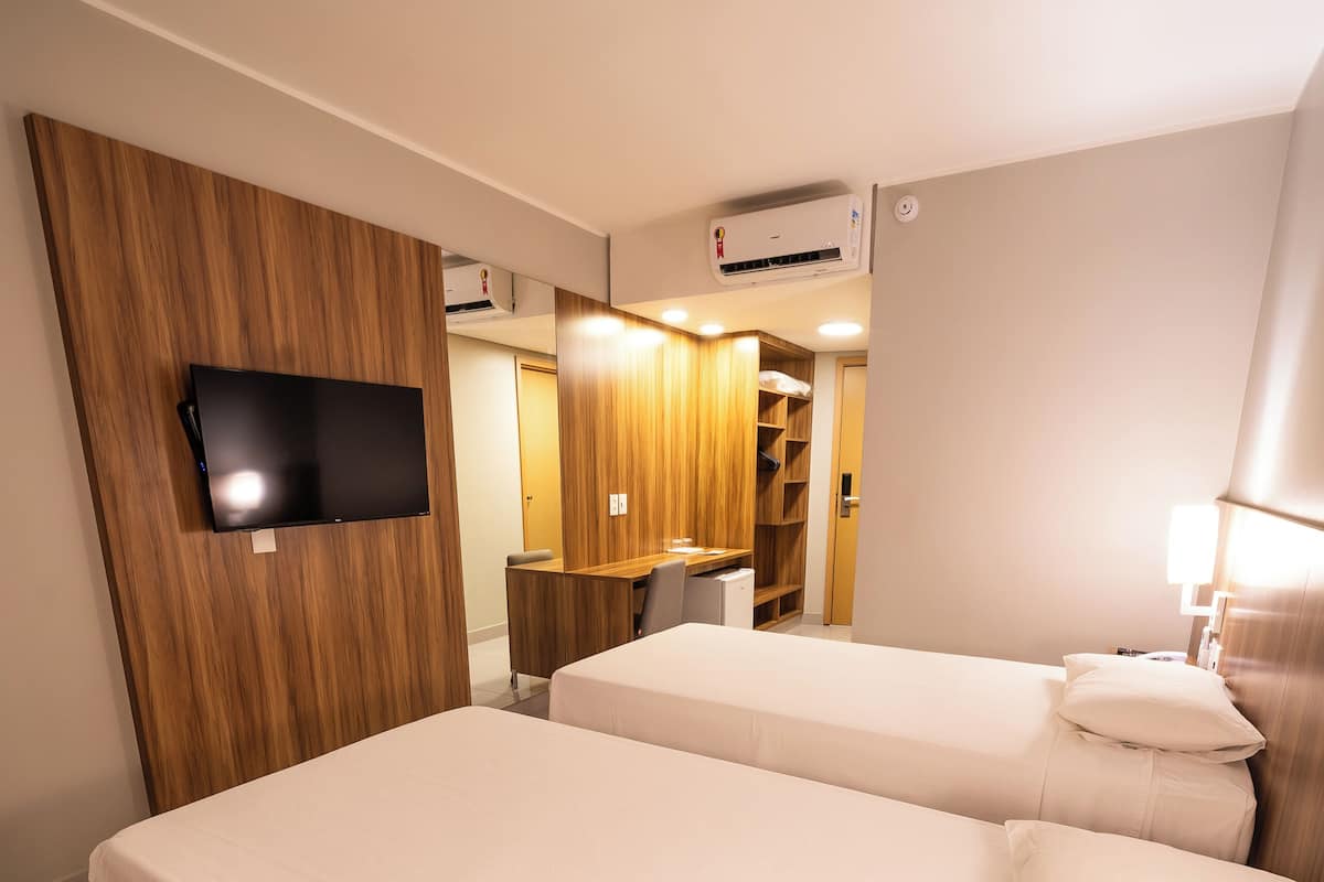 A hotel room with two beds, a TV mounted on the wall, a desk, and a wardrobe.