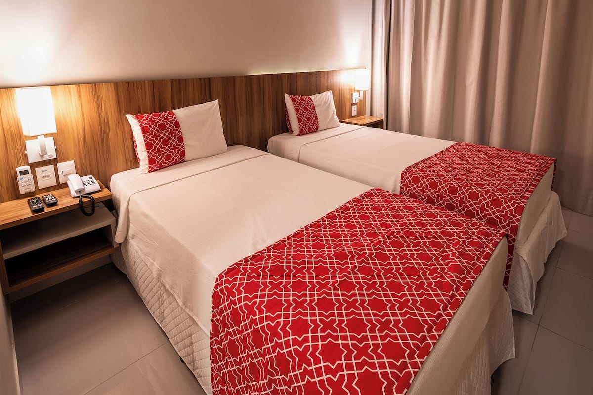 A hotel room with two beds, a bedside table with a lamp, a phone, and a mirror.