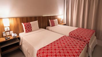 Quarto de hotel com duas camas, uma mesa de cabeceira com abajur, telefone e espelho.