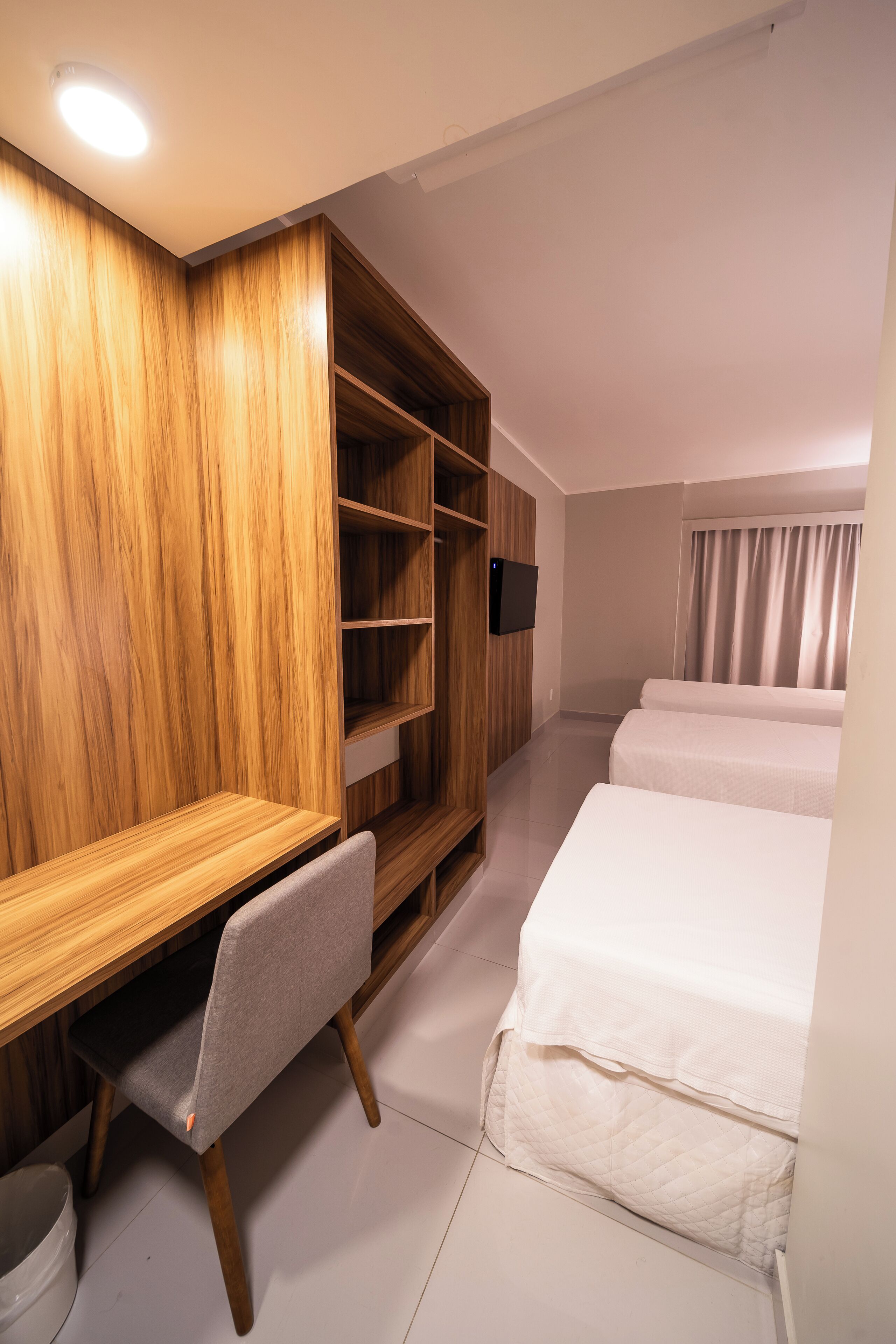 Une chambre d’hôtel avec une armoire en bois, un bureau avec une chaise, deux lits et un téléviseur fixé au mur.