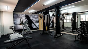 Uma academia com equipamentos de exercícios, esteira e parede com espelhos.
