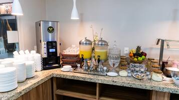 Um balcão de pequeno-almoço com máquina de café, dispensadores de sumo e diversas opções de comida.