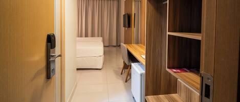 A hotel room with a wooden wardrobe, a bed, a desk, and a television.