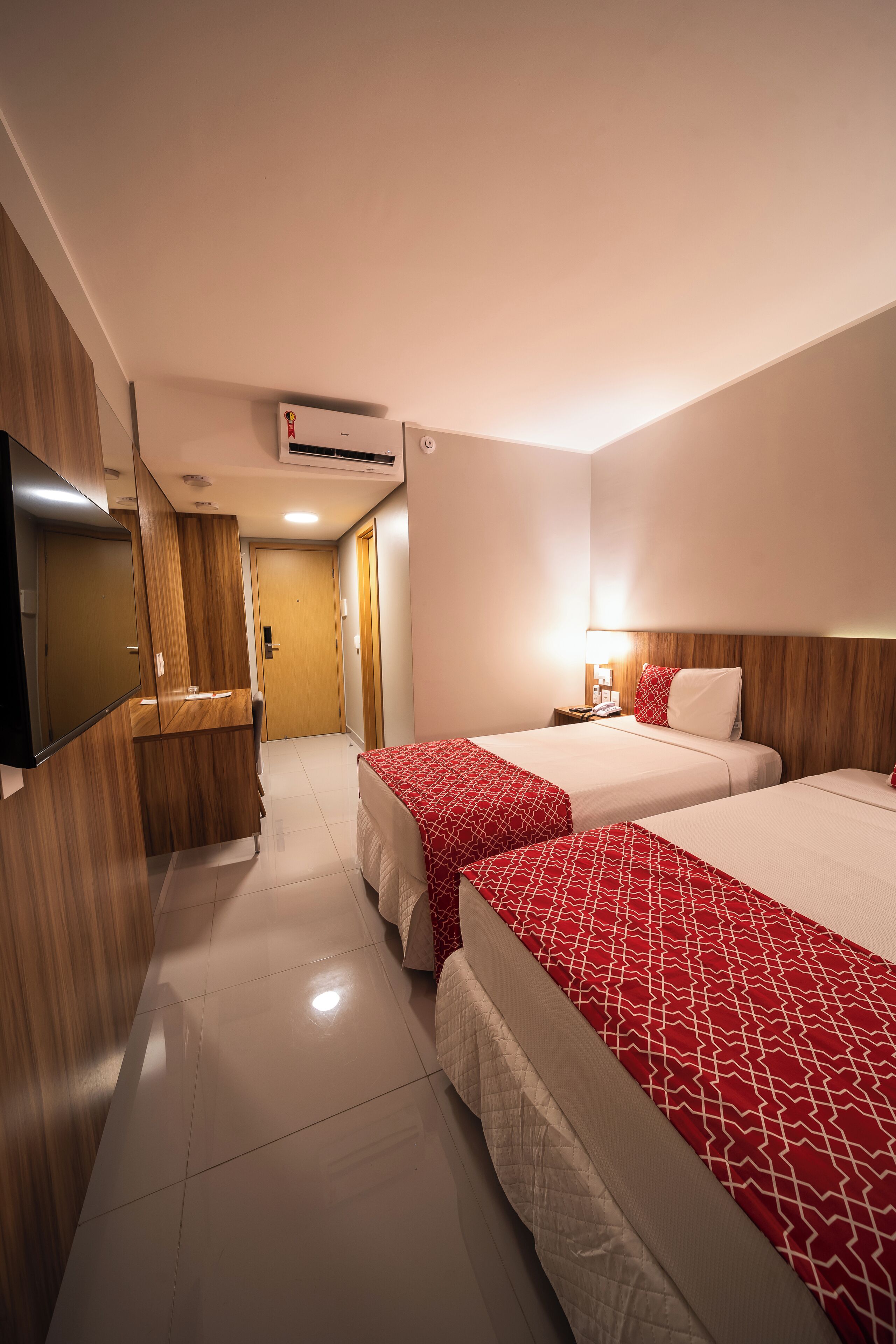 A hotel room with two beds, a TV, a wooden wardrobe, and a bathroom door.
